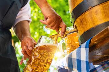 Bavarian man in apron is pouring a large lager beer in tap from wooden beer barrel in the beer garden. Background for Oktoberfest or Wiesn, folk or beer festival (German for: O’zapft is!) - Stock Photo or Stock Video of rcfotostock | RC Photo Stock