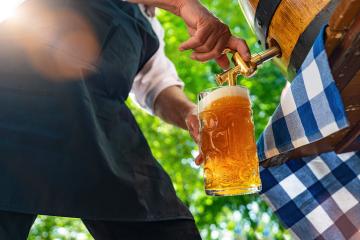 Bavarian man in apron is pouring a large lager beer in tap from wooden beer barrel in the beer garden. Background for Oktoberfest, folk or beer festival (German for: O’zapft is!)  : Stock Photo or Stock Video Download rcfotostock photos, images and assets rcfotostock | RC Photo Stock.: