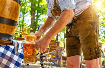 Bavarian man in traditional leather trousers is pouring large lager beers in tap from wooden beer barrel in the beer garden. Background for Oktoberfest or Wiesn, folk or beer festival - Stock Photo or Stock Video of rcfotostock | RC Photo Stock