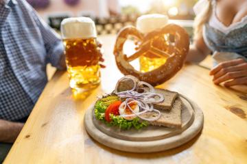 Bavarian Obatzda with pretzels and radishes and beer mugs, man and young woman in tracht in the background at beer garden or oktoberfest, Munich, Germany- Stock Photo or Stock Video of rcfotostock | RC Photo Stock