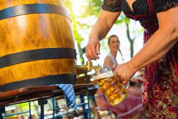 Bavarian Waitress in Tracht, Dirndl  is pouring a large lager beer in tap from wooden beer barrel in the beer garden. Background for Oktoberfest, folk or beer festival (German for: O’zapft is!) - Stock Photo or Stock Video of rcfotostock | RC Photo Stock