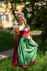 Bavarian woman in traditional german clothing, standing outdoors in a park, holding a beer mug and smiling, wearing a Dirndl with a red bodice and green apron ready for Oktoberfest : Stock Photo or Stock Video Download rcfotostock photos, images and assets rcfotostock | RC Photo Stock.: