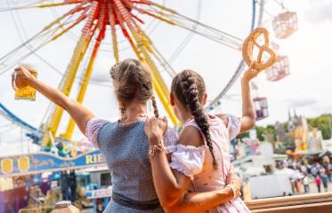 bavarian women in tracht holding a beer mug and pretzel aloft at a lively fairground with Ferris wheel at oktoberfest or duld in germany- Stock Photo or Stock Video of rcfotostock | RC Photo Stock