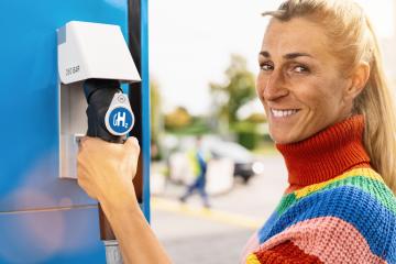 beautiful woman smiling, holds a fuel dispenser with hydrogen logo on gas station to fill up her car. h2 combustion engine for emission free eco friendly transport concept image- Stock Photo or Stock Video of rcfotostock | RC Photo Stock