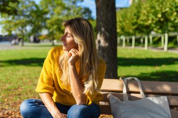 blonde woman sitting outdoor and enjoying the sun on her facce. woman relaxing on a wooden bench with fabric bag under the tree in a summer day. Portrait of woman smiling and daydreaming.- Stock Photo or Stock Video of rcfotostock | RC-Photo-Stock