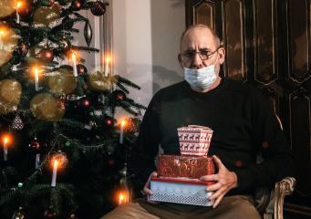 Caucasian Senior man wearing covid-19 mask sitting on chair alone holding a gift in Christmas decorated room . - Stock Photo or Stock Video of rcfotostock | RC Photo Stock