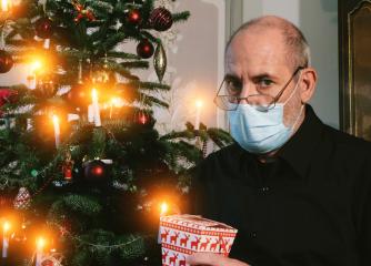 Caucasian Senior man wearing covid-19 mask sitting on chair alone holding a gift in Christmas decorated room .  : Stock Photo or Stock Video Download rcfotostock photos, images and assets rcfotostock | RC Photo Stock.: