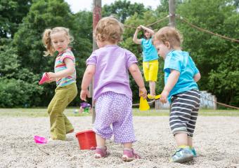 Children playing outdoors in a sandbox, holding toy buckets and shovels, with a child climbing in the background, surrounded by green trees and a summer playground setting : Stock Photo or Stock Video Download rcfotostock photos, images and assets rcfotostock | RC Photo Stock.: