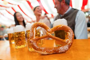 close-up of a large pretzel in front of several mugs of beer, with friends in the background celebrating at Oktoberfest or dult under colorful striped beer tent in munich : Stock Photo or Stock Video Download rcfotostock photos, images and assets rcfotostock | RC Photo Stock.: