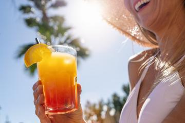 Close-up of a tropical cocktail held by a smiling woman in a straw hat, with a sunlit palm tree backdrop at a Hotel- Stock Photo or Stock Video of rcfotostock | RC Photo Stock