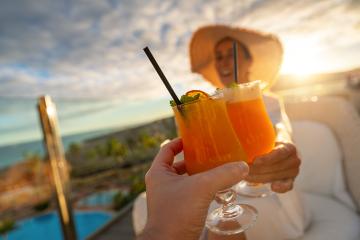 Close-up of a tropical cocktail with a straw held by a woman in a sun hat at tropical beach hotel on sunset- Stock Photo or Stock Video of rcfotostock | RC Photo Stock
