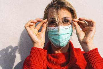 close-up of a woman looks at camera adjusting her round glasses, wearing a turquoise face mask and a red sweater. Corona pandemic safty concept image- Stock Photo or Stock Video of rcfotostock | RC Photo Stock