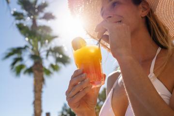 Close-up of a woman sipping a layered tropical cocktail under a straw hat, with sunlit palm trees in the background at caribbean island hotel - Stock Photo or Stock Video of rcfotostock | RC Photo Stock
