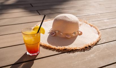 Cocktail with orange slice and straw next to a straw hat on a wooden deck in sunlight at hotel in spain- Stock Photo or Stock Video of rcfotostock | RC Photo Stock