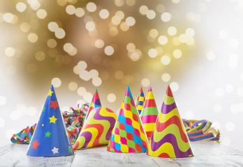 Colorful party hats with vibrant patterns and star designs arranged on a wooden surface, surrounded by festive ribbons, against a warm bokeh light background, creating a celebratory atmosphere : Stock Photo or Stock Video Download rcfotostock photos, images and assets rcfotostock | RC Photo Stock.: