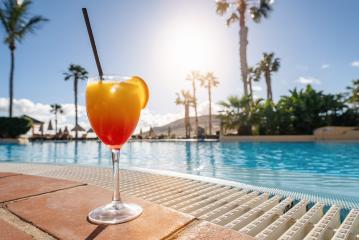 Colorful tropical cocktail on a poolside ledge with a backdrop of palm trees and a bright sunny sky at spanish hotel- Stock Photo or Stock Video of rcfotostock | RC Photo Stock