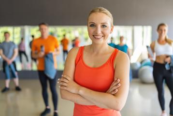 Confident woman in orange tank top standing with arms crossed in a gym. Teamwork Concept image : Stock Photo or Stock Video Download rcfotostock photos, images and assets rcfotostock | RC Photo Stock.: