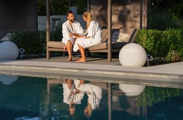 Couple in bathrobes sitting on bench lounger by a pool, reflection in water, outdoor setting in a wellness spa resort - Stock Photo or Stock Video of rcfotostock | RC Photo Stock