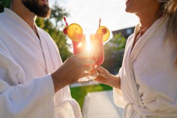 Couple in white bathrobes clinking red cocktails with a sunset behind at spa hotel- Stock Photo or Stock Video of rcfotostock | RC Photo Stock