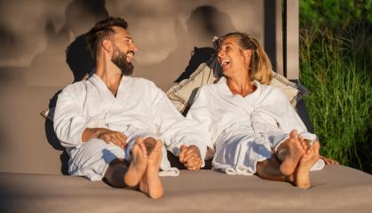 Couple in white bathrobes reclining and enjoying a laugh on a lounger in the sunlight at a spa hotel - Stock Photo or Stock Video of rcfotostock | RC Photo Stock