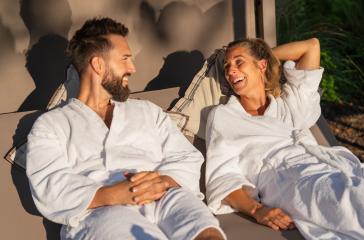Couple in white robes reclining and enjoying a laugh on a lounger in the sunlight at a spa hotel - Stock Photo or Stock Video of rcfotostock | RC Photo Stock