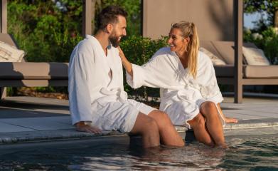Couple in white robes sitting with feet in pool, enjoying a sunny day at spa wellness hotel- Stock Photo or Stock Video of rcfotostock | RC Photo Stock