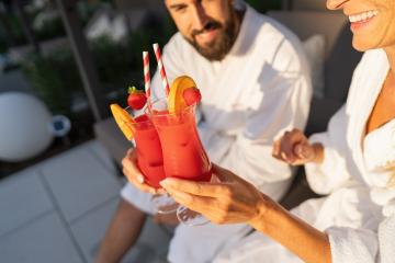 Couple in white robes toasting with fruit garnished cocktails in sunlight at spa hotel- Stock Photo or Stock Video of rcfotostock | RC Photo Stock