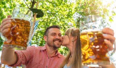 Couple kissing and smiling at camera say cheers or clinking glasses with mug of beer in Bavarian beer garden or oktoberfest- Stock Photo or Stock Video of rcfotostock | RC Photo Stock
