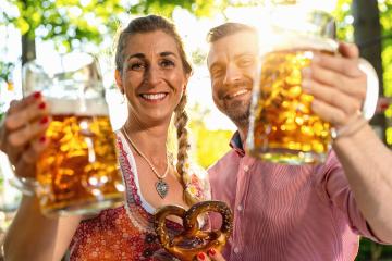 Couple looking and smiling at camera say cheers or clinking glasses with mug of beer in Bavarian beer garden or oktoberfest- Stock Photo or Stock Video of rcfotostock | RC Photo Stock