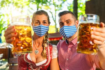 Couple looking with face mask at camera holdingmug of beer glasses in Bavarian beer garden or oktoberfest during covid-19 - Stock Photo or Stock Video of rcfotostock | RC Photo Stock