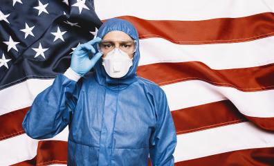 Doctor wearing protection Suit for Fighting Covid-19 (Corona virus) SARS infection Protective Equipment (PPE), Against The American Flag Banner. - Stock Photo or Stock Video of rcfotostock | RC Photo Stock