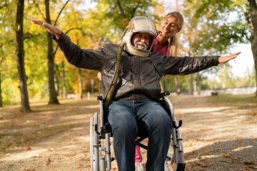 Elderly man in astronaut helmet and leather jacket joyfully extends arms with a nurse, both smiling in an autumn park. Dementia retirement home concept image- Stock Photo or Stock Video of rcfotostock | RC Photo Stock