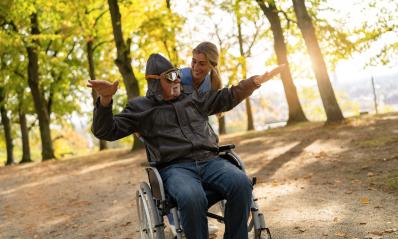 Elderly man in aviator gear and a nurse enjoying a playful moment in a park, with sunlight filtering through autumn trees- Stock Photo or Stock Video of rcfotostock | RC Photo Stock