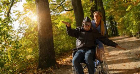 Elderly man in aviator gear extends his arm, mimicking flight, with his nurse assisting, both enjoying a sunlit autumn park- Stock Photo or Stock Video of rcfotostock | RC Photo Stock