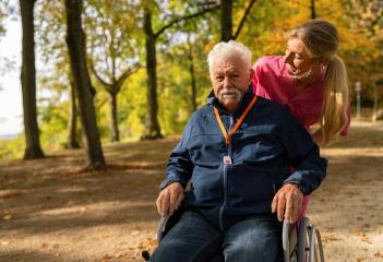 Elderly man in wheelchair outdoors with a caregiver, both smiling, man wearing SOS button. Dementia retirement home concept image- Stock Photo or Stock Video of rcfotostock | RC Photo Stock