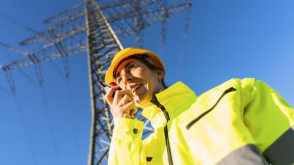 Electrical female engineer talking in a walkie talkie to control a high voltage electricity pylon. Electrical power lines and towers with bright sun- Stock Photo or Stock Video of rcfotostock | RC Photo Stock