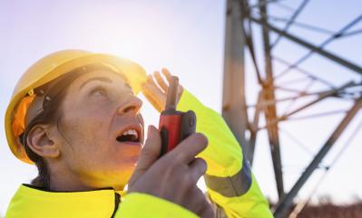 Electrical female engineer watching up and talking in a walkie talkie to control a high voltage electricity pylon. Electrical power lines and towers with bright sun : Stock Photo or Stock Video Download rcfotostock photos, images and assets rcfotostock | RC Photo Stock.: