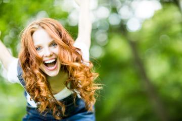 Excited red-haired woman with a big smile outdoors, enjoying a vibrant day in nature with a blurred green background, radiating happiness, energy, and carefree joy in a sunny environment- Stock Photo or Stock Video of rcfotostock | RC Photo Stock