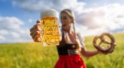 Exuberant woman in Bavarian dress holding a beer mug and pretzel in a sunny wheat field celebrating Oktoberfest festival in munich, germany- Stock Photo or Stock Video of rcfotostock | RC Photo Stock