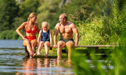 family of three sitting on a dock, dipping their feet in the lake water and enjoying the sunny day- Stock Photo or Stock Video of rcfotostock | RC Photo Stock