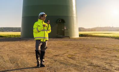 female engineer with safety jacket standing in front of a wind turbine using walkie talkie to checking wind turbine system at a new energy farm- Stock Photo or Stock Video of rcfotostock | RC Photo Stock