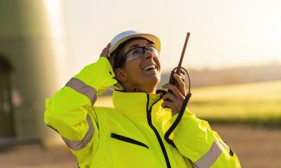 female engineer with safety jacket standing in front of a wind turbine talking in a walkie talkie to checking wind turbine system : Stock Photo or Stock Video Download rcfotostock photos, images and assets rcfotostock | RC Photo Stock.: