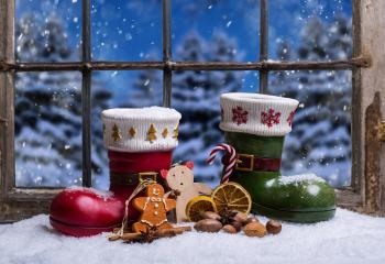 Festive Christmas scene with decorative red and green boots filled with holiday treats, gingerbread, candy cane, dried oranges, nuts, and wooden toys on a snowy windowsill with a snowy forest view : Stock Photo or Stock Video Download rcfotostock photos, images and assets rcfotostock | RC Photo Stock.: