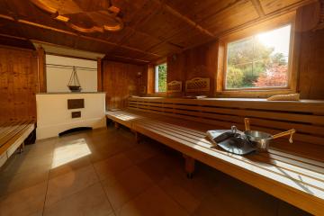 Finnish sauna with tiled floor, wooden benches, stove, towel, metal bucket, ladle, and felt hats with window with a view in a spa hotel- Stock Photo or Stock Video of rcfotostock | RC Photo Stock