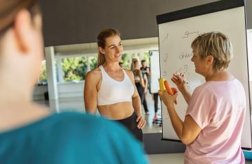 Fitness class with a woman writing on a whiteboard about nutritional advice holding a banana, apple and a carrot, focusing on nutrition- Stock Photo or Stock Video of rcfotostock | RC Photo Stock