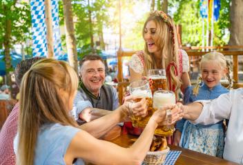friends and family in Tracht, Dirndl and Lederhosen having fun sitting on table drinking beer and eating pretzels in Beer garden or oktoberfest in Bavaria, Germany- Stock Photo or Stock Video of rcfotostock | RC Photo Stock