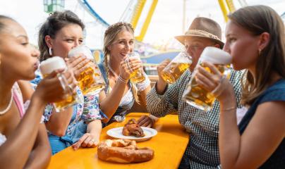 Friends enjoying bavarian beer at oktoberfest festival on a beer tent table with a pretzel and grilled chicken, amusement rides visible- Stock Photo or Stock Video of rcfotostock | RC Photo Stock