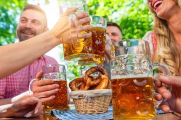 friends in Tracht, Dirndl and Lederhosen having fun sitting on table drinking beer and eating pretzels in Beer garden or oktoberfest in Bavaria, Germany- Stock Photo or Stock Video of rcfotostock | RC Photo Stock