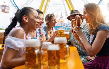 Friends laughing and sharing beer and pretzels at a festival tent table, amusement rides visible in the background at oktoberfest in munich or dult in germany- Stock Photo or Stock Video of rcfotostock | RC Photo Stock