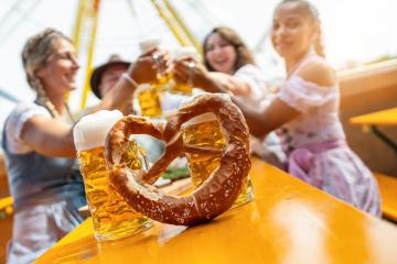 Friends sharing laughs and toasts with beer and a pretzel at a sunny fairground at oktoberfest or duld in germany- Stock Photo or Stock Video of rcfotostock | RC Photo Stock
